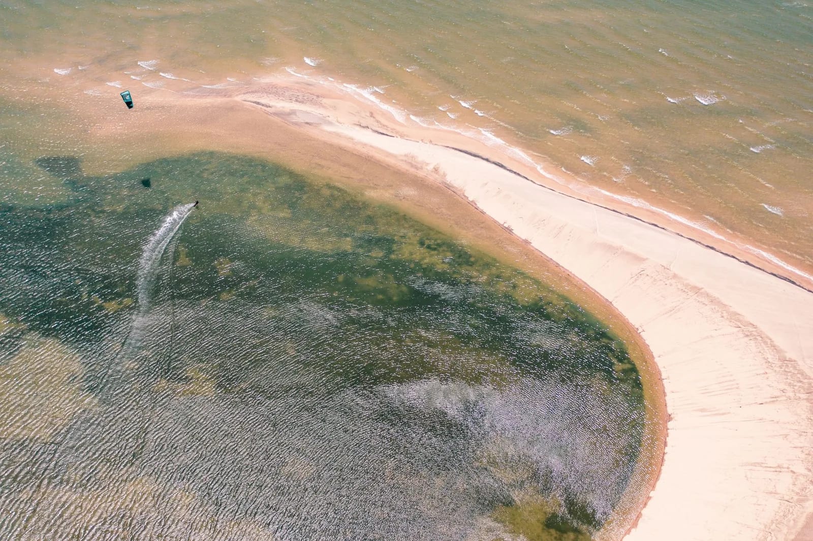 Vue aérienne d'un kitesurfeur sur un plan d'eau plat abrité par une longue flèche de sable