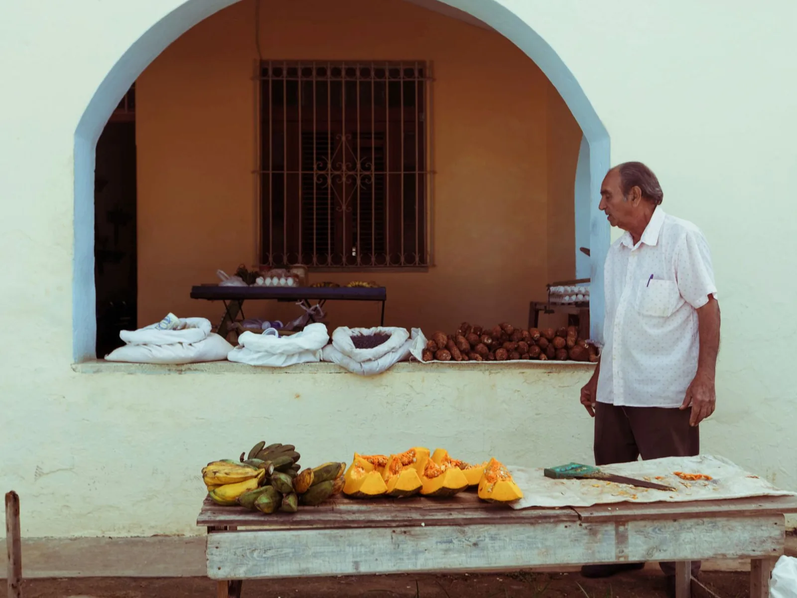 Homme âgé devant un étal de bananes et de courges dans un village panaméen