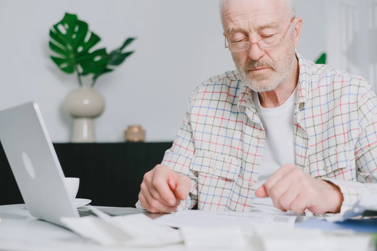 Homme âgé examinant des relevés de pension papier devant un ordinateur portable