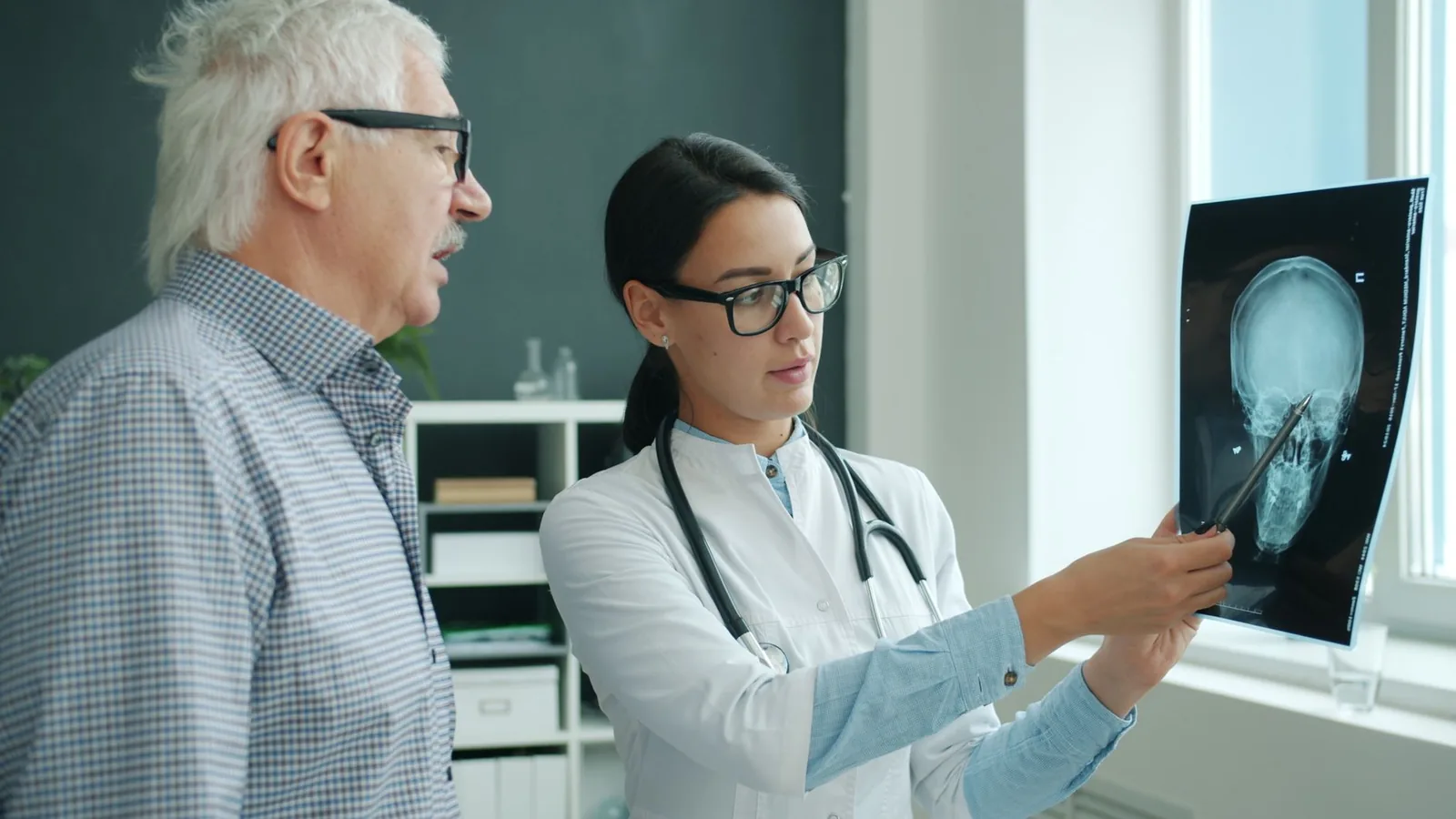 Médecin commentant une radiographie du crâne devant un patient âgé lors d'une consultation